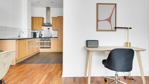 A modern kitchen with wooden cabinets, a stove, and a coffee maker. There is a desk with a chair and a framed picture on the wall. - Charming Old Street 1BR, 5 min walk to Old Street Tube, by Blueground (London)