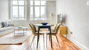 A modern living room with a sofa, a coffee table, a dining table with chairs, a floor lamp, and a TV. - Charming Old Street 1BR, 5 min walk to Old Street Tube, by Blueground (London)