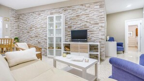 Ein Wohnzimmer mit einer Steinwand, einem Fernseher auf einem Standfuß, einem weißen Couchtisch und zwei Sofas.