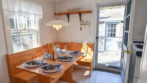 A dining area with a wooden table set for four, a hanging light fixture, and a view through a glass door to the outside.