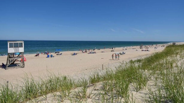 A beach with a lifeguard tower, people sunbathing, and a clear blue sky.