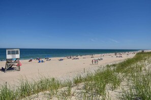Une plage avec un poste de surveillance pour les sauveteurs, des gens qui prennent un bain de soleil et un ciel bleu dégagé.