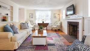 A living room with a sofa, armchairs, a coffee table, a fireplace, and a television mounted above it.