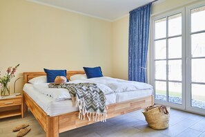 Une chambre avec un lit en bois, du linge de lit blanc, un rideau bleu et une vue sur l’extérieur.