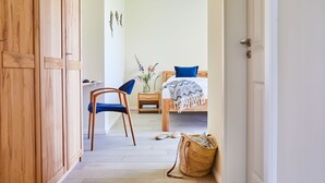 A hallway leading to a bedroom with a bed, a chair, a small table, and a basket. - Vacation home Graukranich 41 - Holiday home Graukranich 41 - Close to nature (Fuhlendorf)