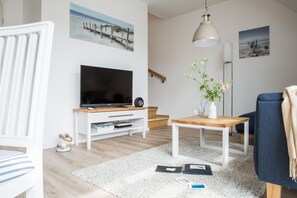 A modern living room with a flat-screen TV, wooden coffee table, and a white sofa.