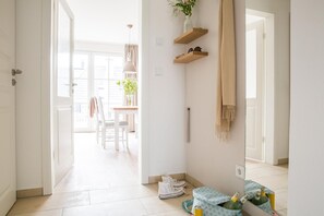 A bright hallway with a dining area in the background, a wooden door, and a small table with a bag and bottles.