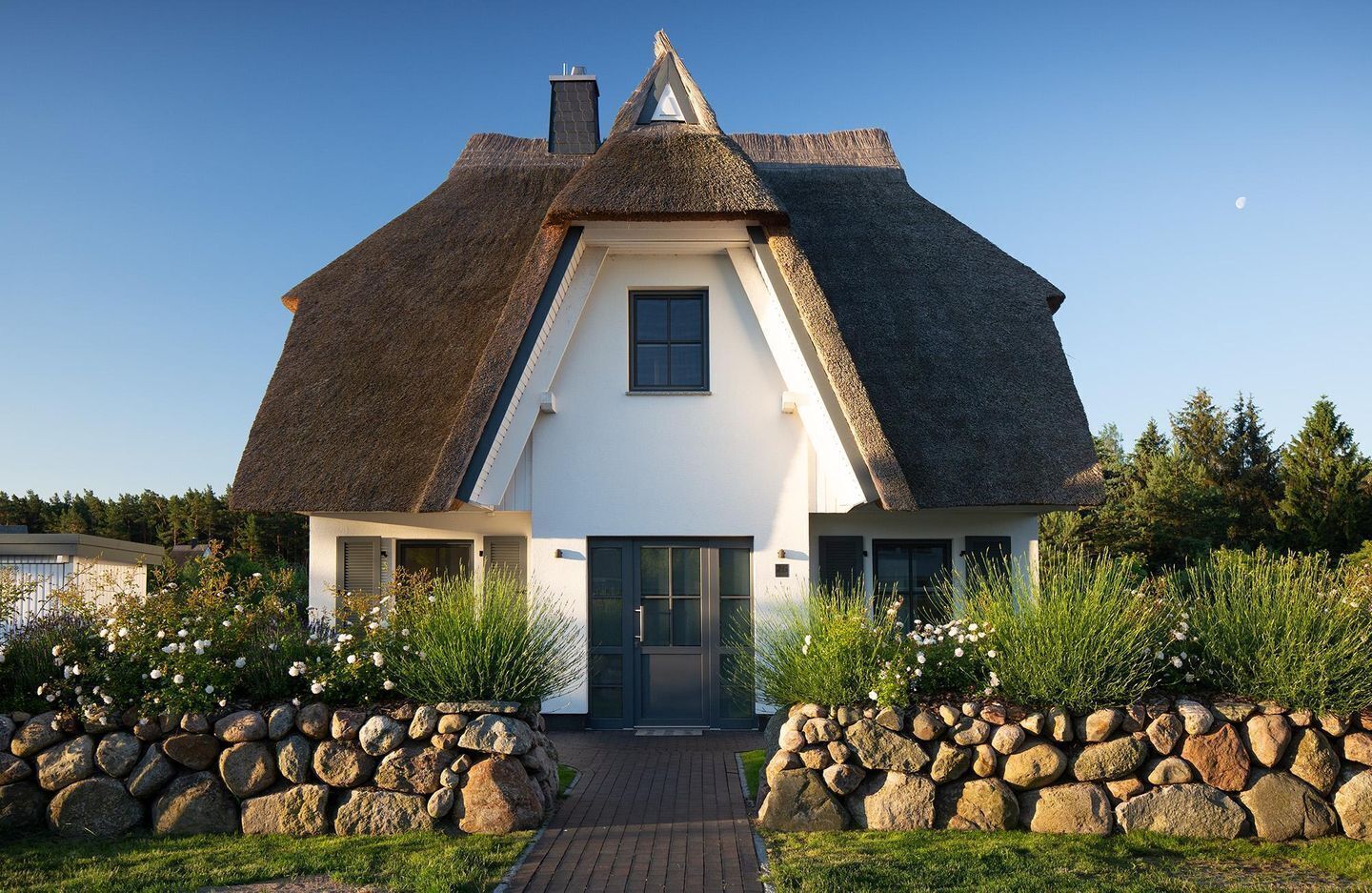 A house with a steeply pitched thatched roof, white exterior walls, and a central door.