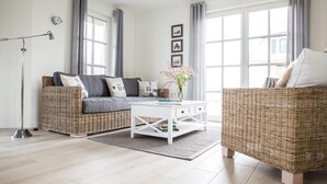 A modern living room with a grey sofa, white coffee table, and wicker furniture. - Vacation home Seeschwalbe 44 - Holiday home Seeschwalbe 44 - Close to nature (Fuhlendorf)