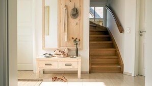 Eine Holztreppe führt zu einer oberen Etage, eine Holzbank mit einem Blumenstrauß und ein Spiegel mit einem hängenden Topf.