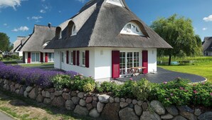 Ein traditionelles Haus mit Strohdach, einer Steinmauer und Blumenbeeten davor.