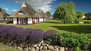 Ein reetgedecktes Cottage mit roter Tür, umgeben von einem gepflegten Rasen und Lavendelsträuchern.