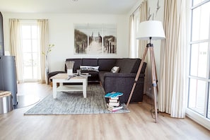 Un salon moderne avec un canapé, une table basse, une lampe et une grande fenêtre avec des rideaux.