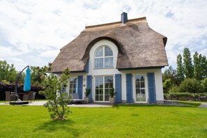 Una casa con tetto di paglia, ampie finestre e un prato curato.