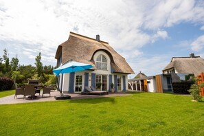 A house with a large lawn, a patio with outdoor furniture, and a thatched roof.