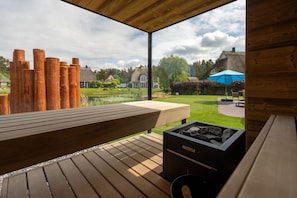 Una terraza de madera con una parrilla y vistas a un jardín y casas.