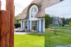 A house with a thatched roof, a large arched window, and a well-maintained lawn.
