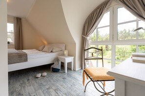 Ein Schlafzimmer mit Bett, Nachttisch, Stuhl und einem Fenster mit Blick auf Grünflächen.