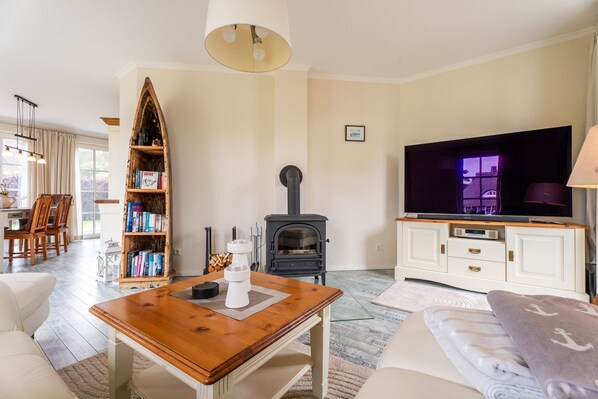 A cozy living room with a fireplace, a television, a bookshelf, and a dining area.