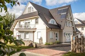 Une maison à deux étages avec un balcon, des panneaux solaires et une allée pavée en briques.