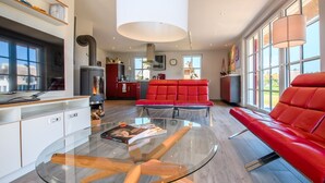 Una sala de estar moderna con una mesa de centro de vidrio, un sofá rojo y una zona de cocina con estufa y armarios.