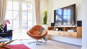 Moderni olohuone, jossa on nahkainen nojatuoli, lasinen sohvapöytä, punainen matto, puinen TV-taso ja suuri litteänäyttöinen televisio.