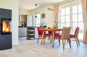 A modern kitchen with a built-in fireplace, a dining area with red upholstered chairs, and a large window providing natural light.