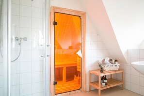 A modern bathroom with a wooden sauna door, a shower, and a wooden shelf with toiletries.