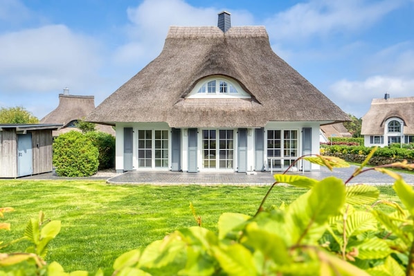 Une maison au toit de chaume, dotée d’un grand porche à l’avant et d’une pelouse bien entretenue.