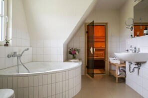 Ein modernes Badezimmer mit einer großzügigen freistehenden Badewanne, einer gläsernen begehbaren Dusche und einem weißen Waschbecken mit Spiegel.