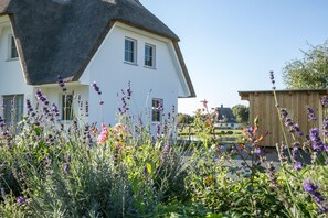 Una casa blanca con techo negro, rodeada de un jardín con lavanda y otras flores.