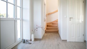 Een hal met een houten trap, witte muren en een raam.