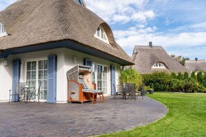 Un bâtiment à toit de chaume doté d’un patio, de sièges extérieurs et d’une pelouse bien entretenue.