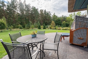 A patio with a round table and chairs, a grill, and a view of a forested area.