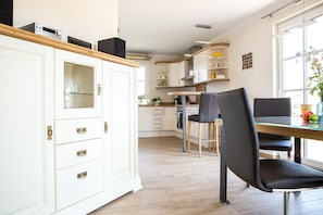 A modern kitchen with white cabinetry, a dining area with a glass table, and a black chair.