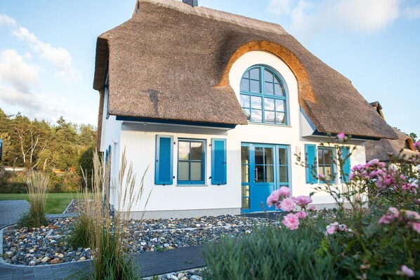 Ein Haus mit Strohdach, weißen Wänden und blauen Fensterläden.