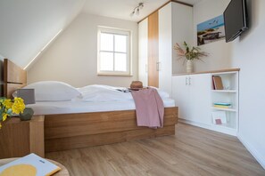 Un dormitorio con una cama de madera, una mesita de noche con lámpara, una ventana, un televisor y una estantería.