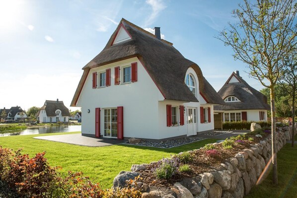 A house with a steeply pitched roof, white exterior walls, and red shutters.