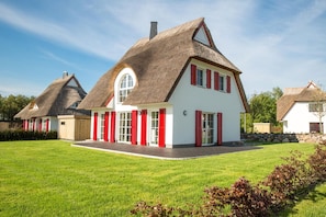 Ein traditionelles Haus mit einem Strohdach, weißen Wänden und roten Fensterläden.