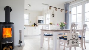Una sala de estar acogedora con una estufa de leña, un comedor con mesa y sillas, y una cocina al fondo.