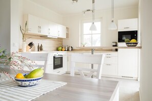Una cocina moderna con armarios blancos, horno integrado, microondas y comedor con mesa y sillas.