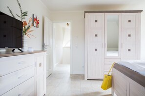 Un dormitorio con cama, armario, televisor y un pasillo que conduce a otra habitación.