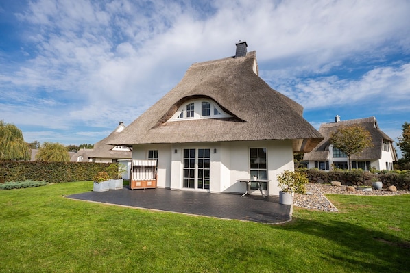 A thatched-roof house with a paved driveway and a well-maintained lawn.