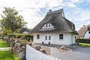 Ein traditionelles Haus mit Strohdach und weißem Anstrich, umgeben von einer Steinmauer und einem weißen Zäunchen.