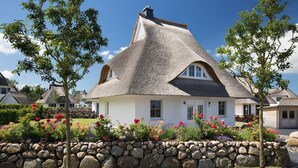 Una casa con techo de paja, pared de piedra y jardín de flores.