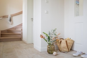 Un pasillo limpio y minimalista con una escalera de madera, un jarrón con flores, una cesta tejida y un par de zapatillas deportivas.
