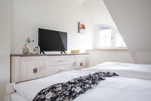Un dormitorio con cama, televisor sobre una cómoda, una ventana y un cuadro.