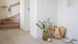 Un pasillo limpio y minimalista con una escalera de madera, un jarrón con flores, una cesta tejida y un par de zapatillas deportivas.