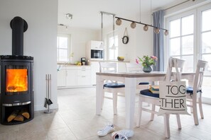 Una sala de estar acogedora con una estufa de leña, un comedor con mesa y sillas, y una cocina al fondo.