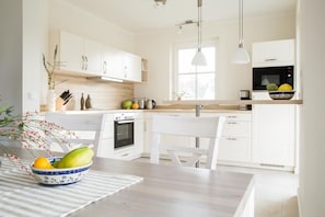 Une cuisine moderne avec des meubles blancs, un four encastré, un four à micro-ondes et un coin repas comprenant une table et des chaises.
